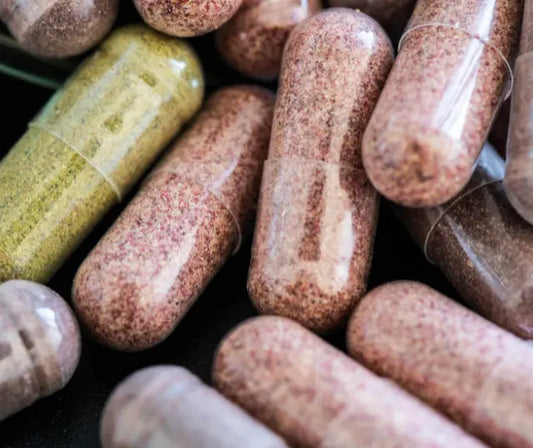 Young broccoli sprouts, blackcurrant skins, gold and green kiwifruit beside four open plant-based supplement capsules